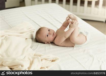 Little baby lying on bed and holding feet