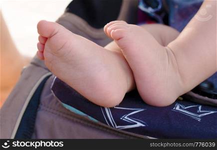 Little beautiful baby feet lying in a stroller while walking in a summer park
