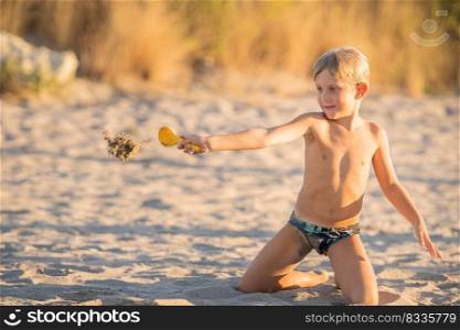 Little blond boy playing with small colorful plastic sand toy on the beach, kid building a sandcastle with fun, active happy summer holiday.
