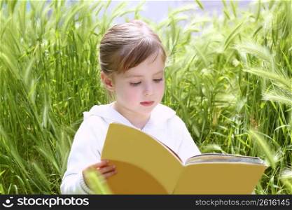 little blond girl reading book between green spikes meadow garden