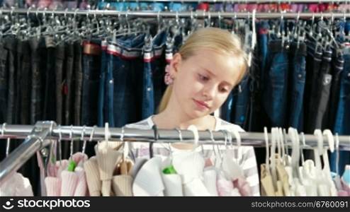 Little blond girl shopping for clothes in a clothing store, looking sweater. Front view