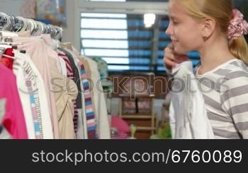 Little blond girl shopping for clothes in a clothing store, looking sweater. Side view
