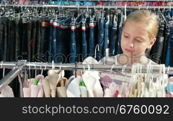 Little blond girl shopping for clothes in a clothing store, trying on sweater. Front view