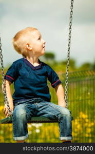 Little blonde boy having fun at the playground. Child kid playing on a swing outdoor. Happy active childhood.