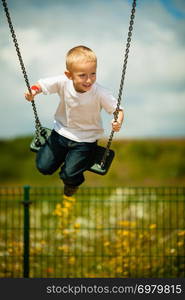 Little blonde boy having fun at the playground. Child kid playing on a swing outdoor. Happy active childhood.