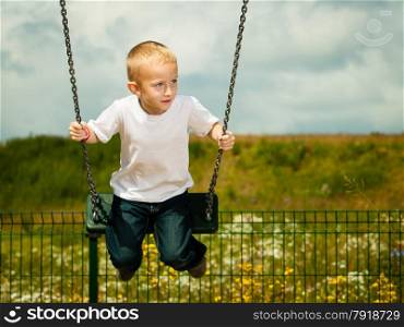 Little blonde boy having fun at the playground. Child kid playing on a swing outdoor. Happy active childhood.
