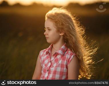 Little blonde child girl standing in summer field at sunset.. Little blonde child girl standing in summer field at sunset