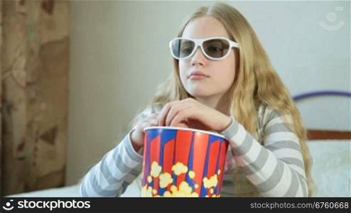Little blonde girl eating popcorn and watching 3D TV at home