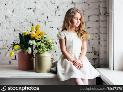 Little blonde girl in a white dress sitting by the window. Little blonde girl in a white dress sitting by the window.