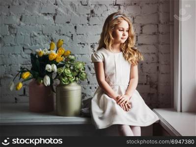 Little blonde girl in a white dress sitting by the window. Little blonde girl in a white dress sitting by the window.