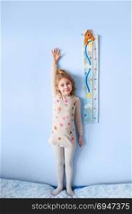 Little blonde girl measuring height against wall in room. Little blonde girl measuring height against wall in room.