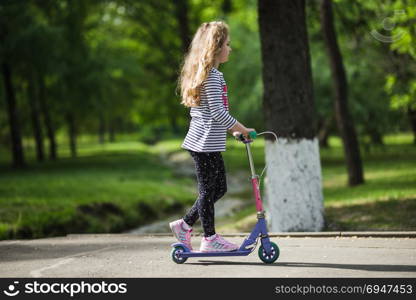 Little blonde girl ride the scooter in the park.. Little blonde girl ride the scooter in the park