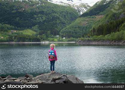 little blonde girl standing at the shore of norwegian lake