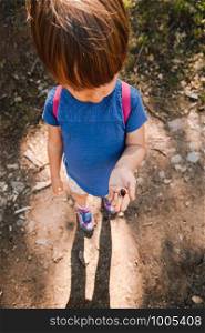 Little blonde girl with acorns in her hand in the forest path with backpack