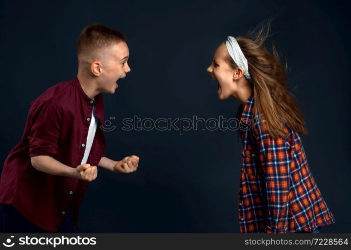 Little boy and girl are shouting at each other in studio, developing hair effect. Children and wind, kids isolated on dark background, child emotion. Little boy and girl are shouting, developing hair