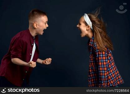 Little boy and girl are shouting at each other in studio, developing hair effect. Children and wind, kids isolated on dark background, child emotion. Little boy and girl are shouting, developing hair