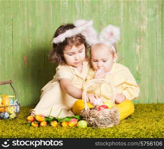 Little boy and girl as a Easter rabbits on the grass with colorful eggs. Easter rabbits