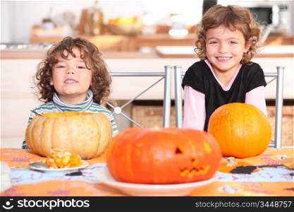 little boy and girl dressed in pajamas posing behind pumpkins