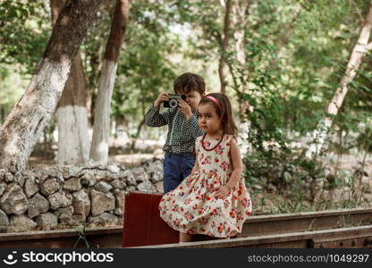 little boy and girl in vintage clothes with vintage suitcase and with vintage camera on abandoned railway