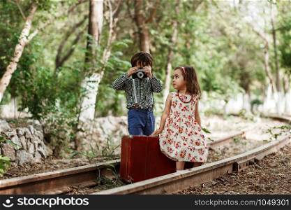 little boy and girl in vintage clothes with vintage suitcase and with vintage camera on abandoned railway