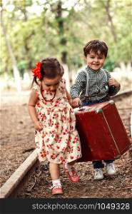 little boy and girl in vintage clothes with vintage suitcase and with vintage camera on abandoned railway