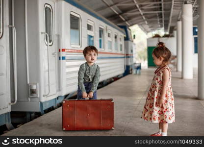 little boy and girl in vintage clothes with vintage suitcase at small railway station