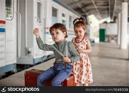 little boy and girl in vintage clothes with vintage suitcase at small railway station