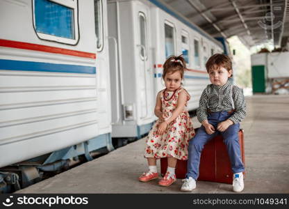 little boy and girl in vintage clothes with vintage suitcase at small railway station