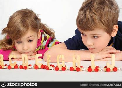 little boy and girl lying on floor and playing with wooden alphabet railway, focus on boy, boy looking at gir