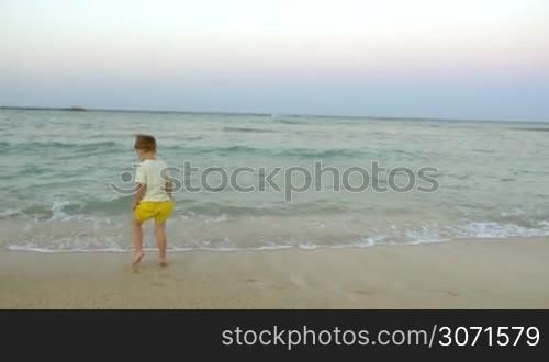 Little boy and his father jumping in surf water on the beach. Having great time on vacation with family at the seaside