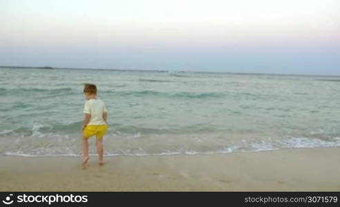 Little boy and his father jumping in surf water on the beach. Having great time on vacation with family at the seaside