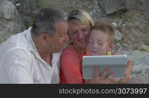 Little boy and his grandparents are watching something in tablet.