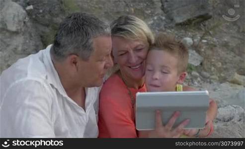 Little boy and his grandparents are watching something in tablet.