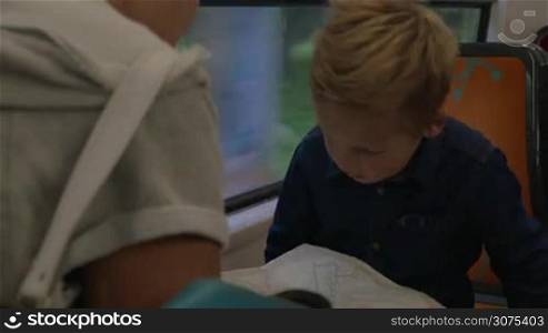 Little boy and mother riding in the train and searching travel destination on the map