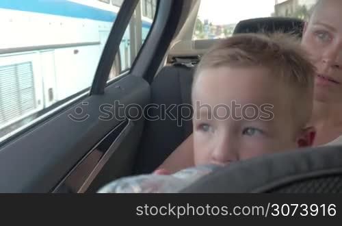 Little boy and mother travelling in car. Boy drinking from bottle, kissing mother and looking through the window