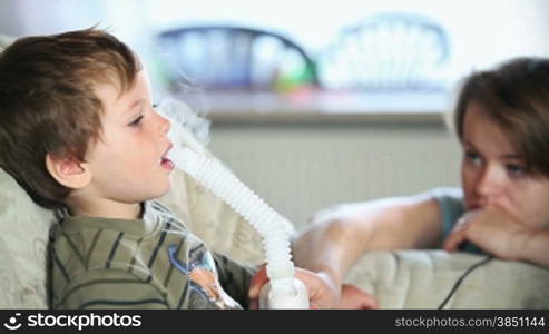 Little boy and mother using nebulizer to inhale medicine
