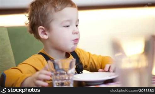 Little boy at the table in cafe eating, he choosing food and mother giving it to him right into the mouth