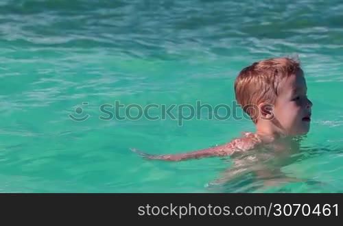 Little boy bathing alone in clear blue sea and talking to somedody