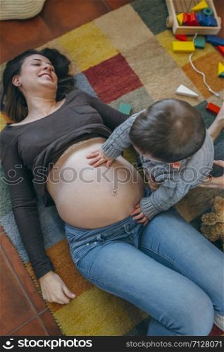 Little boy caressing belly of his pregnant mother. Toddler caressing belly of his pregnant mother