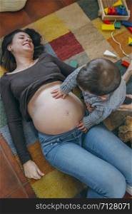 Little boy caressing belly of his pregnant mother. Toddler caressing belly of his pregnant mother