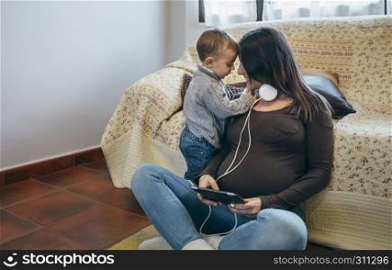 Little boy claiming the attention of his pregnant mother in the living room. Toddler claiming the attention of his pregnant mother