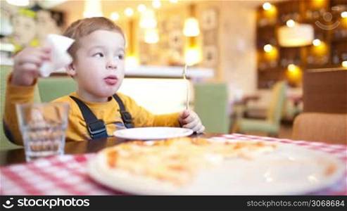 Little boy cleaning his face with napkin, then mother taking a slice of pizza for herself and giving a small piece to her son
