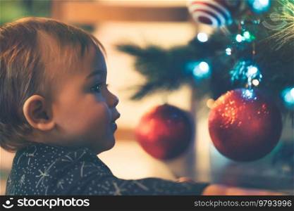 Little boy decorates Christmas tree, happy child awaiting for a Xmas miracle, nice cozy New Year night at home. Little boy decorates Christmas tree