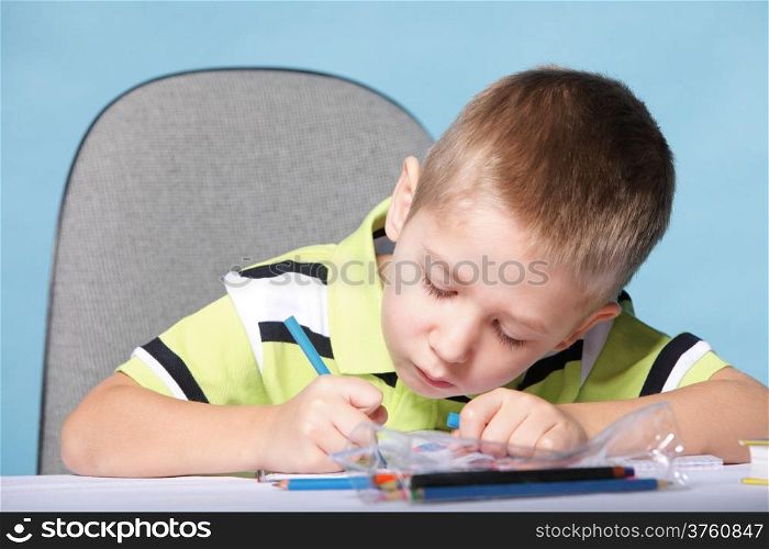 little boy drawing with color pencils on blue background