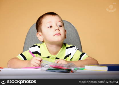 little boy drawing with color pencils on orange background