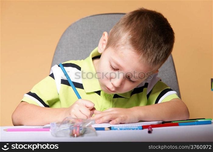 little boy drawing with color pencils on orange background