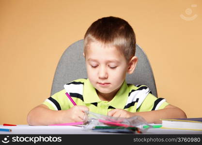 little boy drawing with color pencils on orange background