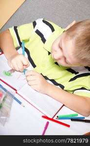 little boy drawing with color pencils on orange background