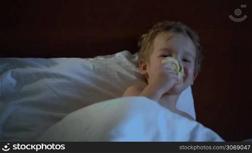 Little boy eating a bun in bed during watching TV