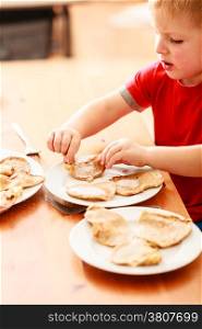 Little boy eating fried apple in pancake dough or apple fritters pancakes with icing sugar at home